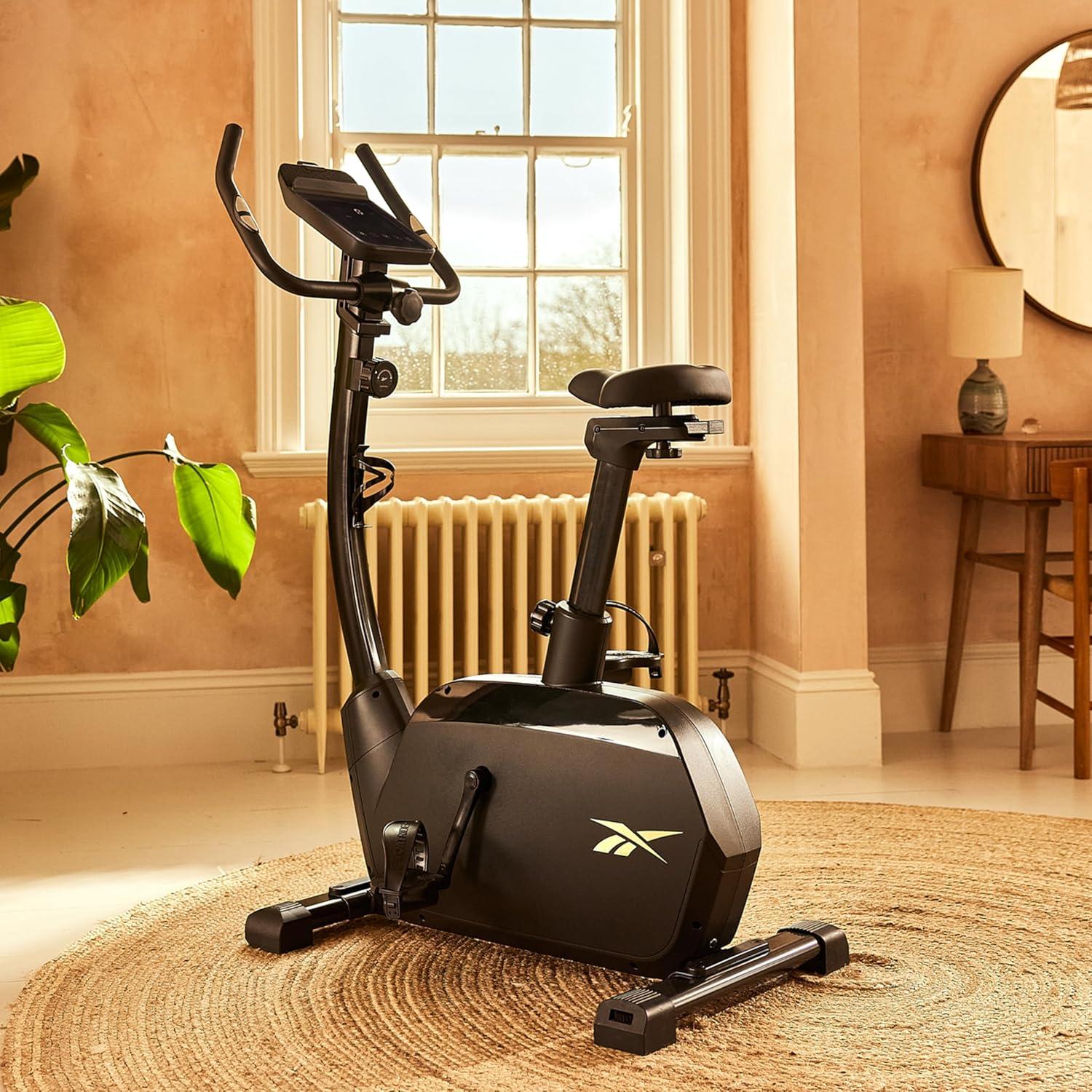 imageReebok Fitness Stationary Bike Bluetooth Compatible Indoor Cycling Bike 24 Resistance Levels 12 Workouts Upright Exercise Bike with Gel Pad SaddleBlackFR20