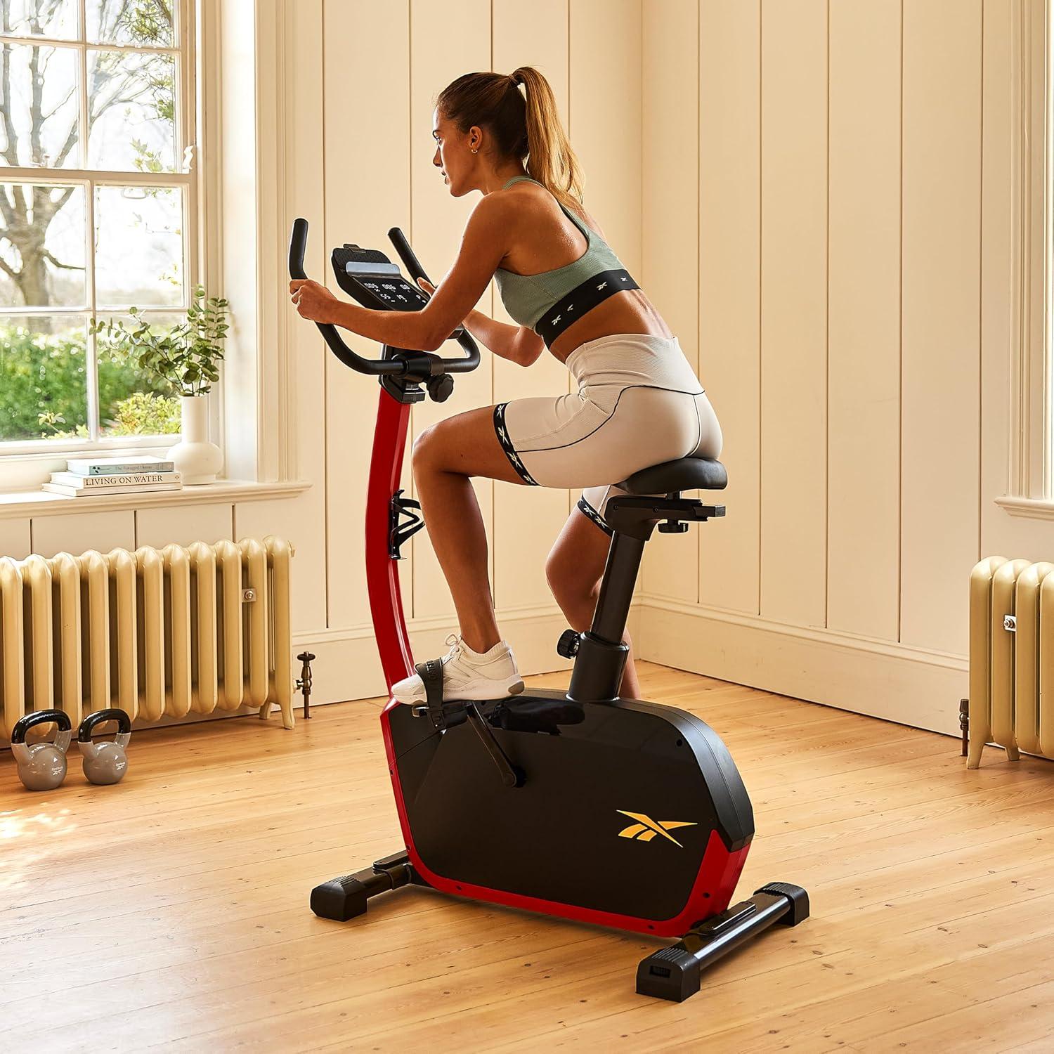 imageReebok Fitness Stationary Bike Bluetooth Compatible Indoor Cycling Bike 24 Resistance Levels 12 Workouts Upright Exercise Bike with Gel Pad SaddleRed