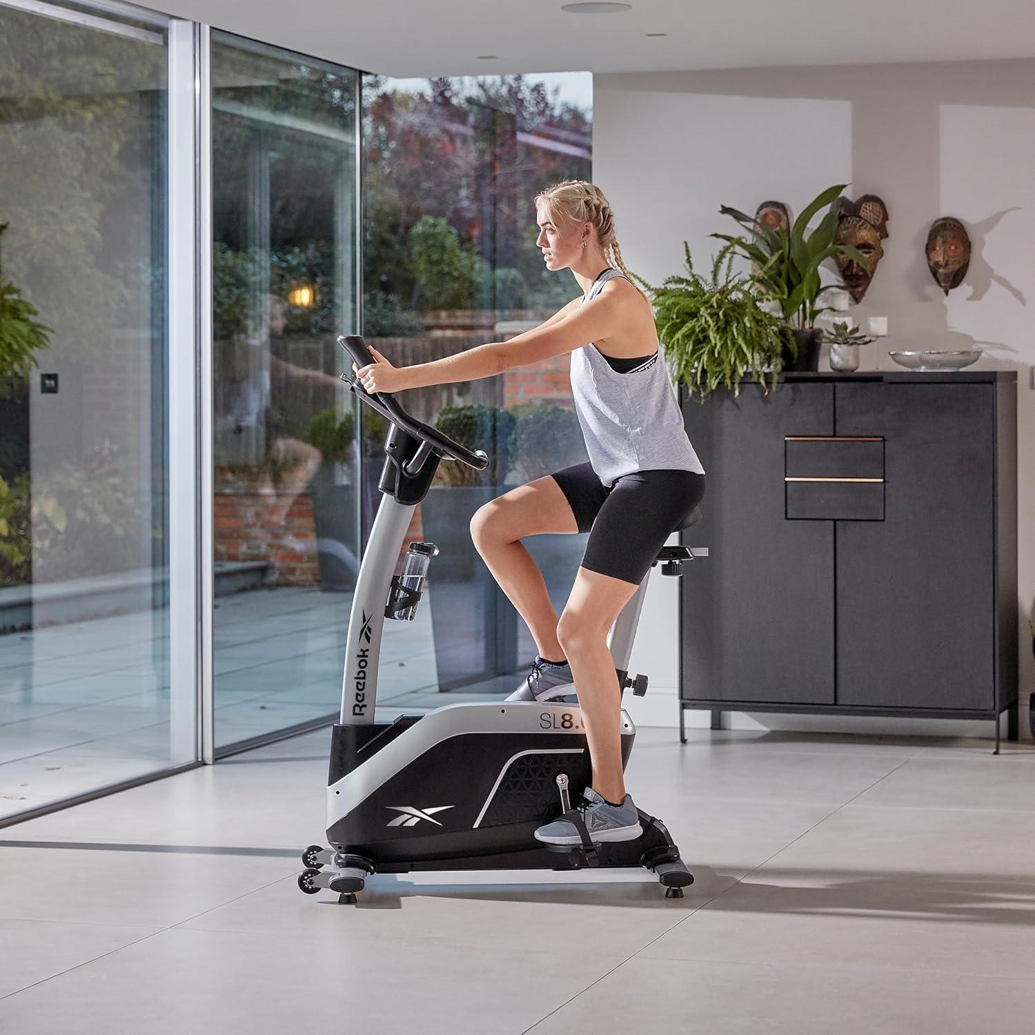 imageReebok Fitness Stationary Bike Bluetooth Compatible Indoor Cycling Bike 24 Resistance Levels 12 Workouts Upright Exercise Bike with Gel Pad SaddleSilver