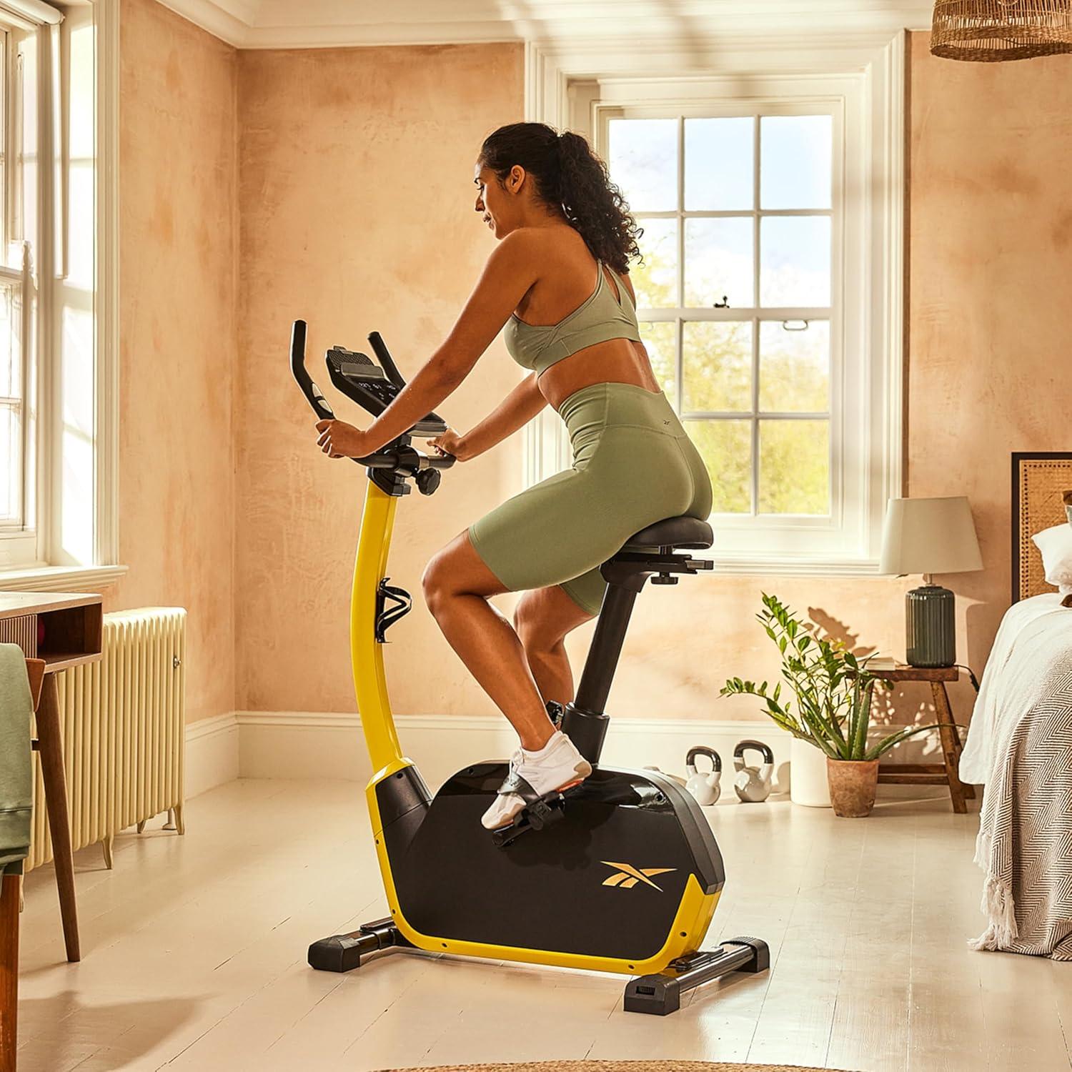 imageReebok Fitness Stationary Bike Bluetooth Compatible Indoor Cycling Bike 24 Resistance Levels 12 Workouts Upright Exercise Bike with Gel Pad SaddleYellow